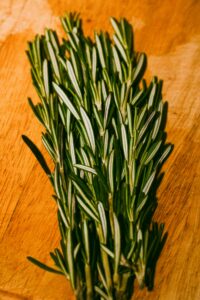 Close-up of fresh rosemary sprigs on a wooden board, showcasing vibrant herbs.