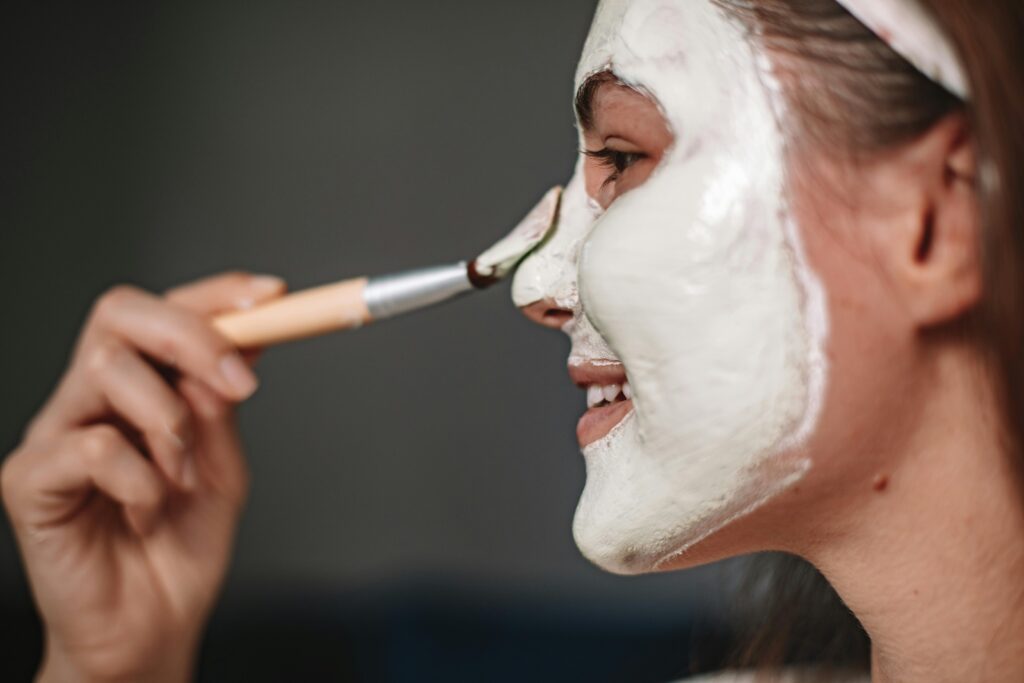 Smiling woman applying a facial mask with a brush, focusing on skincare and wellness.