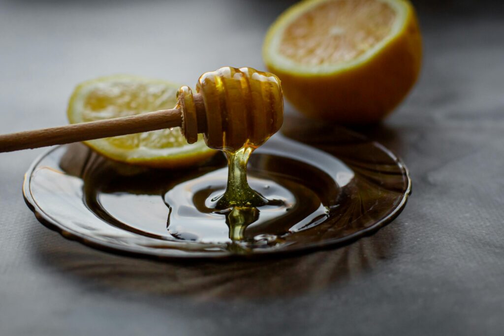 Delicious honey flowing down from dipper into saucer with lemon slice placed on black table