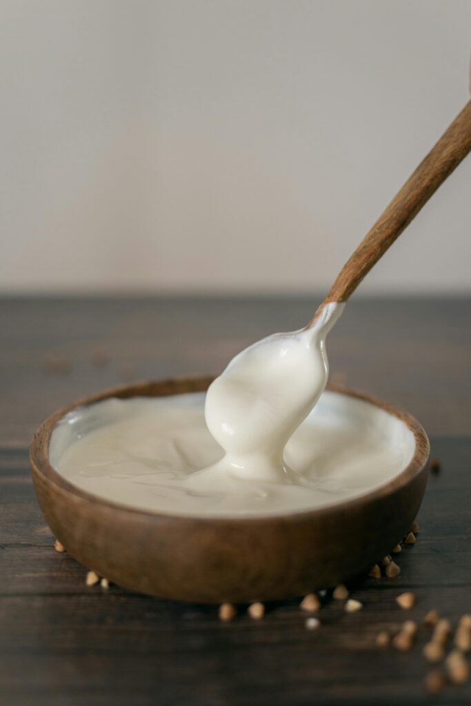 From above of anonymous person stirring yoghurt with spoon in wooden bowl placed on table against blurred background