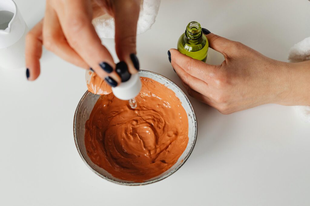 Close-up of hands blending clay mask with skincare essence in minimalist setting.