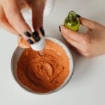 Close-up of hands blending clay mask with skincare essence in minimalist setting.