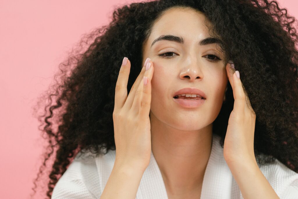 A young woman with curly hair applies skincare products, emphasizing a healthy facial routine.