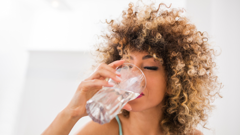a woman drinking water from a glass, which helps her skin to glow and stay healthy.