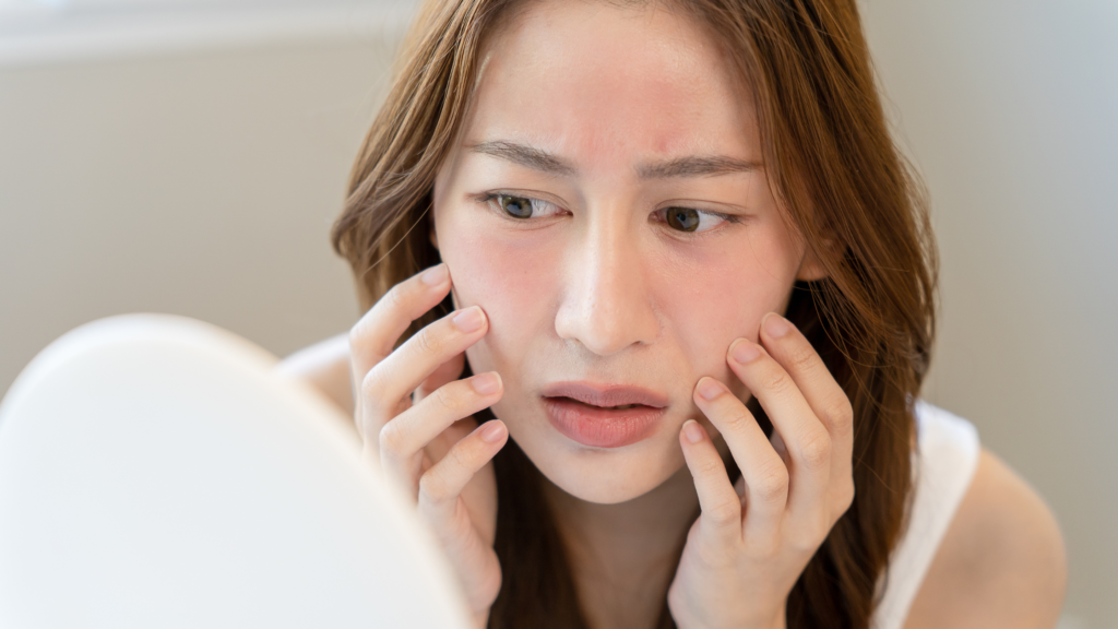 A woman with sensitive skin looks at herself in the mirror, observing how rough her skin has become