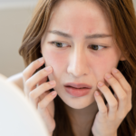 A woman with sensitive skin looks at herself in the mirror, observing how rough her skin has become