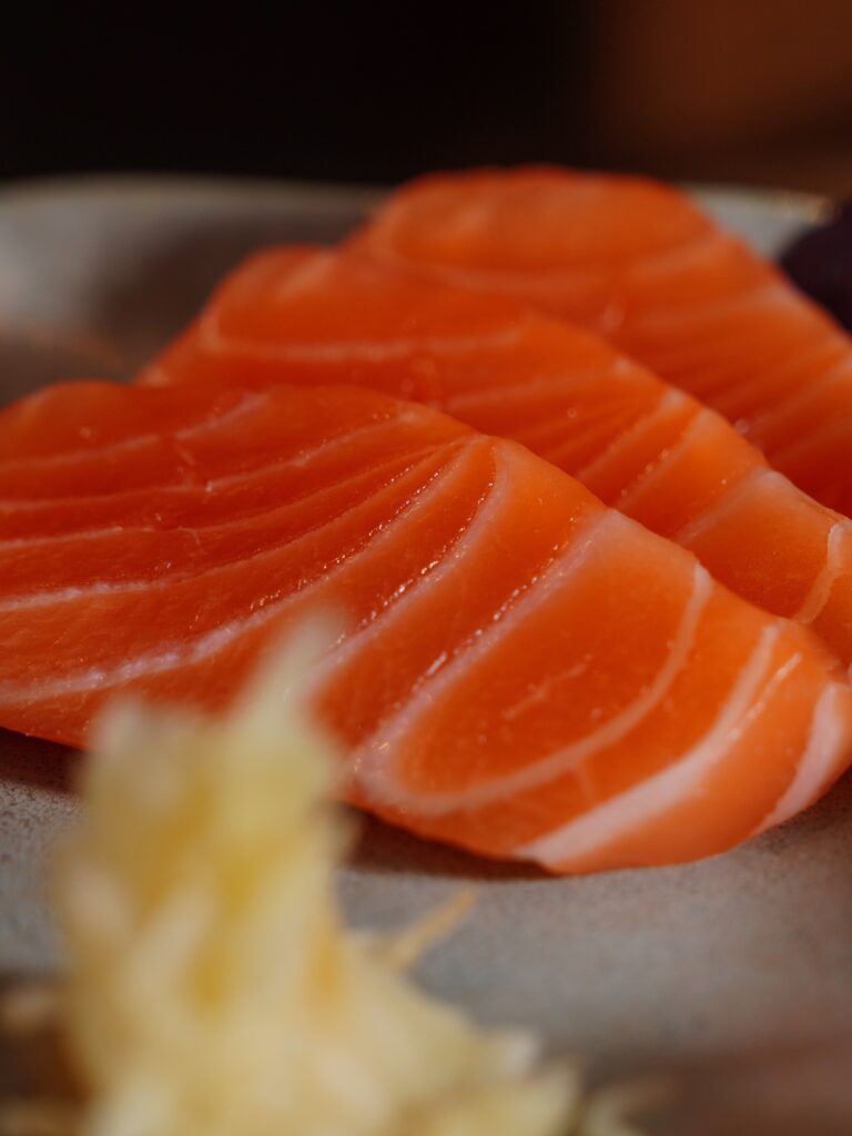 Fresh, raw salmon slices displayed on a plate in a vertical shot.