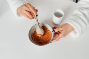 Top view of a woman mixing a skincare mask with a spoon in a bowl, highlighting a beauty routine.